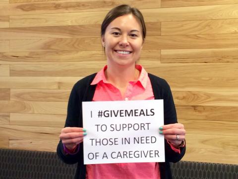 A volunteer holding a "I #givemeals ..." sign